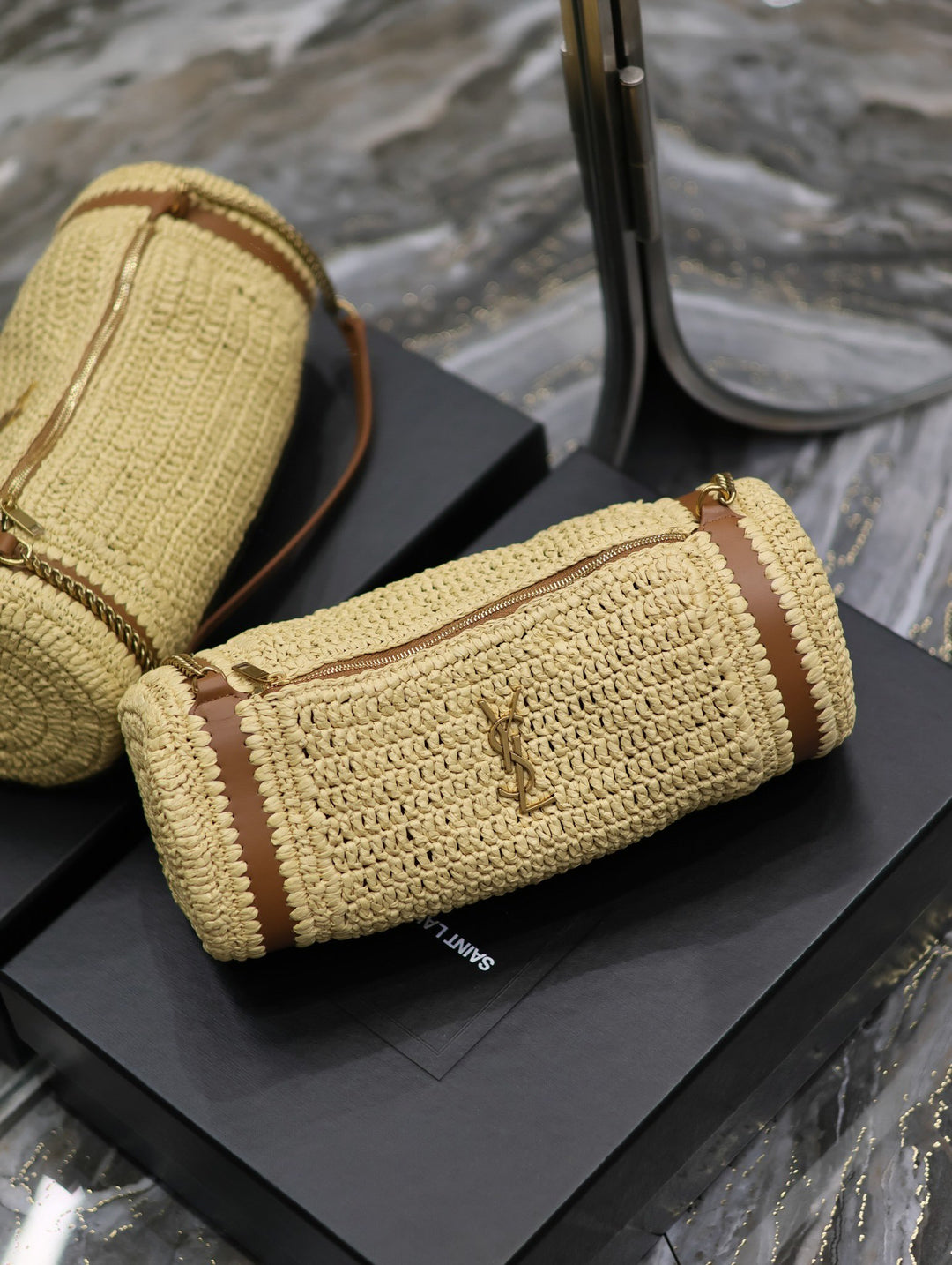 Cassandre raffia cylinder bag front view showing monogram hardware and zip closure detail

