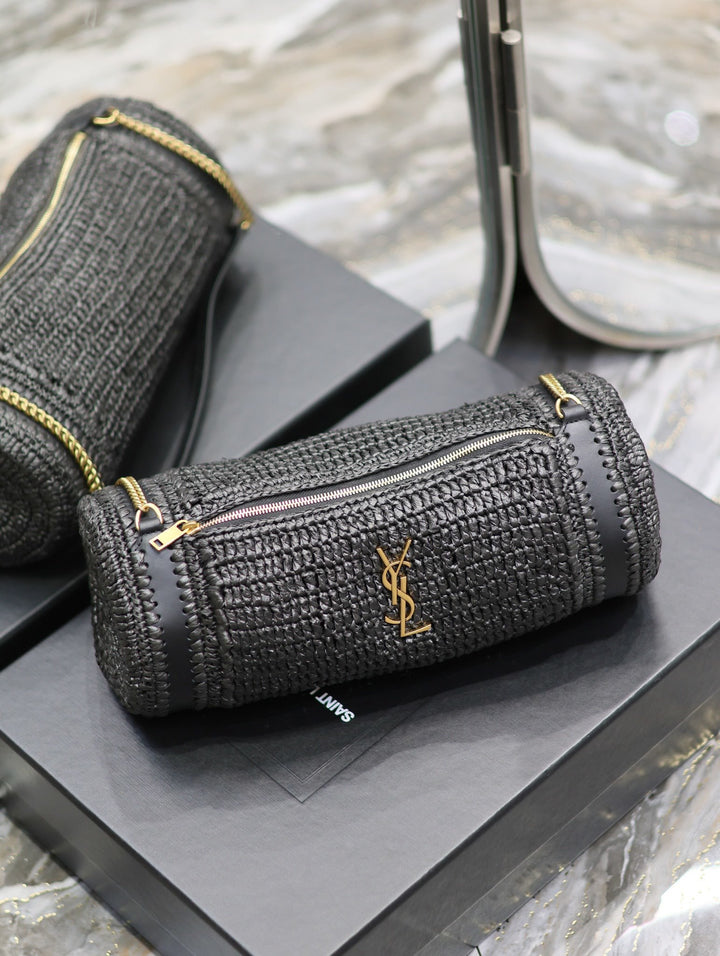 Natural raffia cylindrical bag with bronze chain strap coiled on dark marble surface
