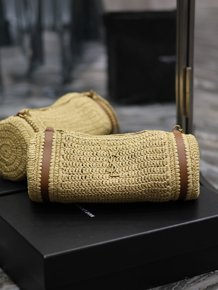 Raffia cylinder crossbody bag side view showing tan leather barrel end trim detail
