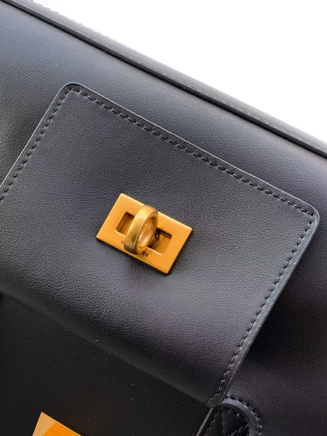 Black handbag with a gold clasp on a light gray background