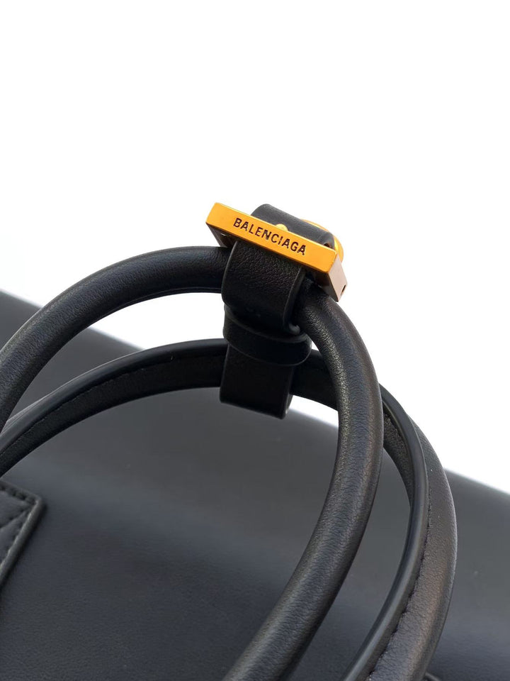 Close-up of a black leather bag with a yellow Balenciaga tag on a white background
