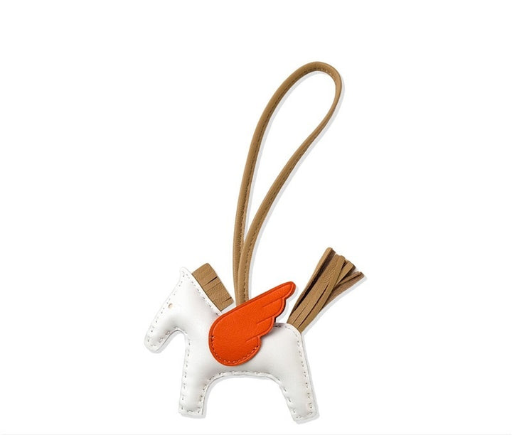 White horse-shaped keychain with orange wings and brown strap on a white background