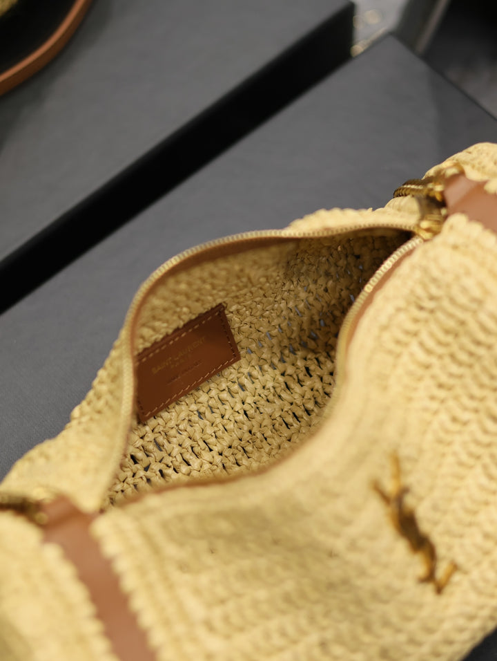 Beige raffia roll bag with gold chain shoulder strap lifestyle shot on minimalist surface
