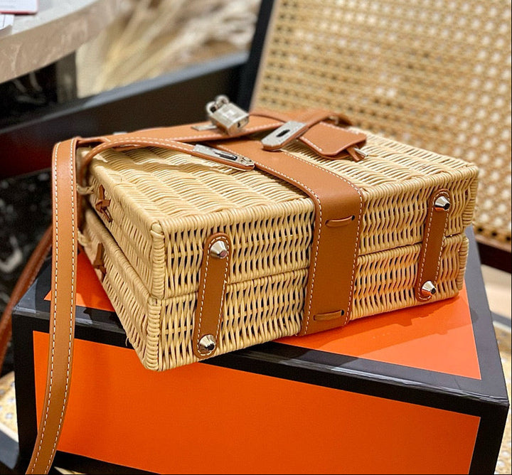Wicker picnic basket with brown leather straps on an orange surface