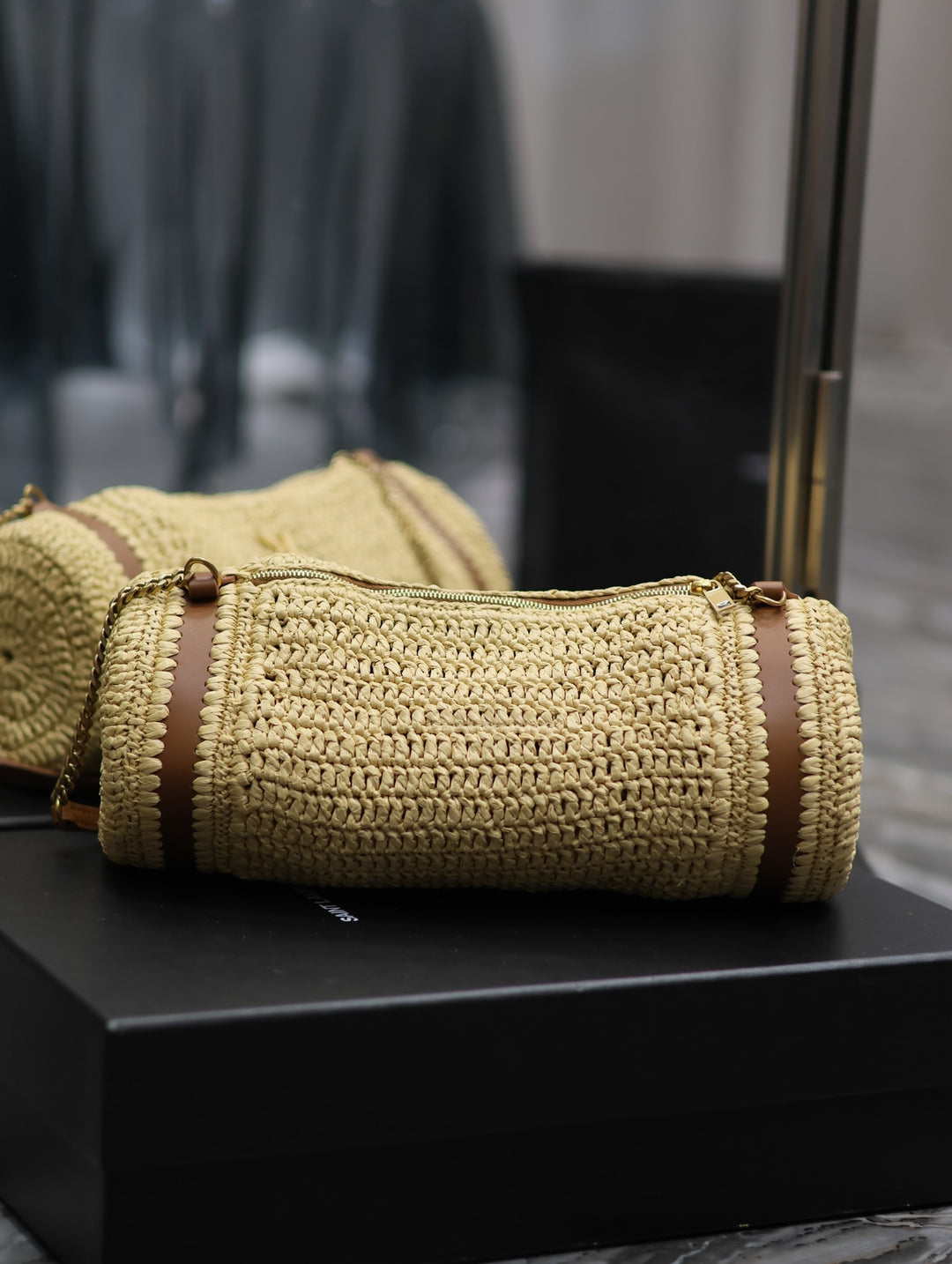 Namrico braided raffia cylinder bag with tan leather trim flat lay on textured surface
