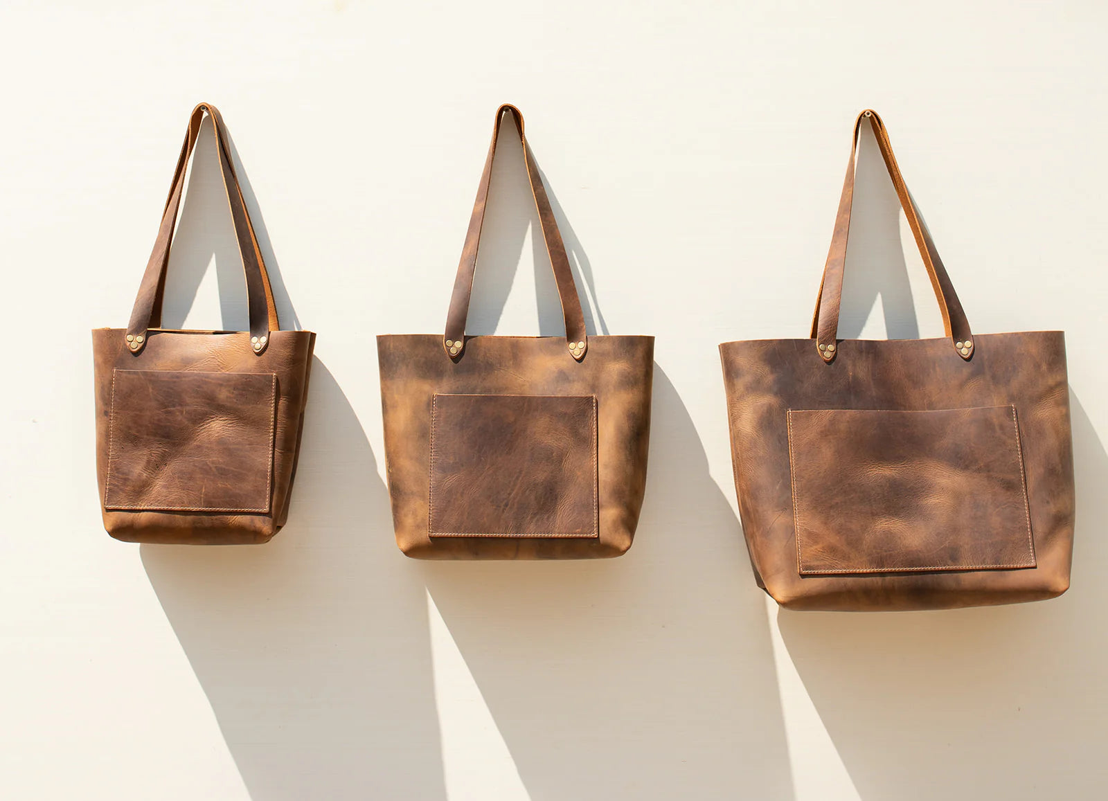 Three brown leather tote bags on a white background