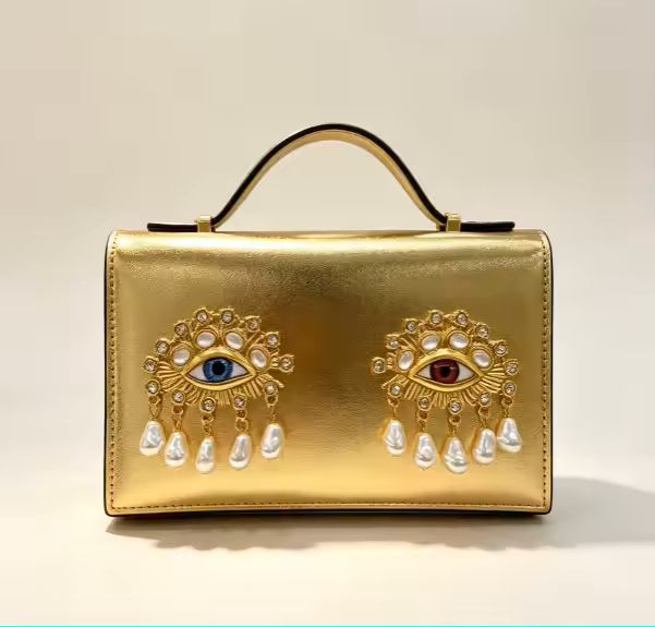 Burgundy small square crossbody bag with 3D jewel eye and pearl detail on white background