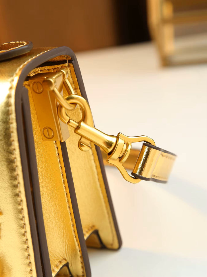 Close-up detail of a metallic gold handbag showing the interior lining, gold-tone hardware, and a gold-and-black strap attachment.