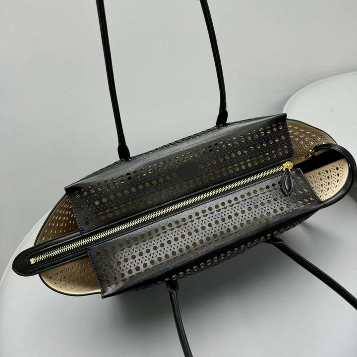 Black perforated handbag with gold zipper on a white surface