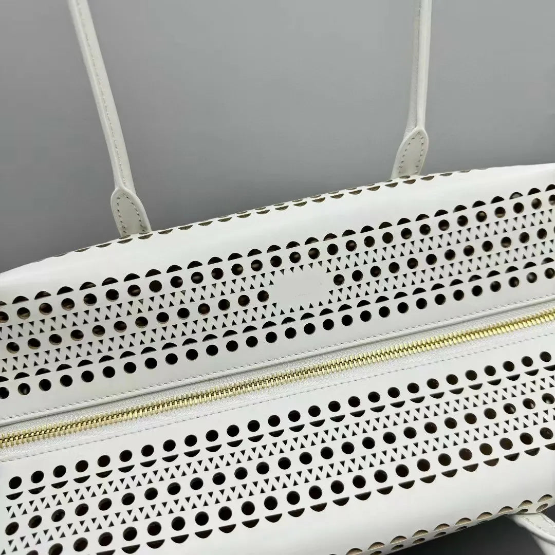 White handbag with perforated design and gold zipper on a gray background