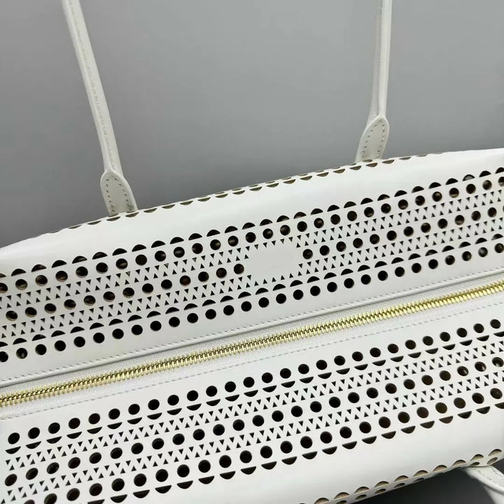 White handbag with perforated design and gold zipper on a gray background