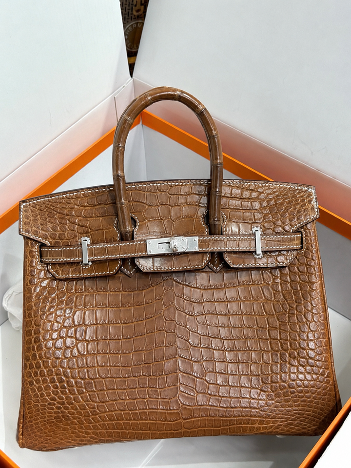 Brown crocodile skin handbag with silver hardware on a white background