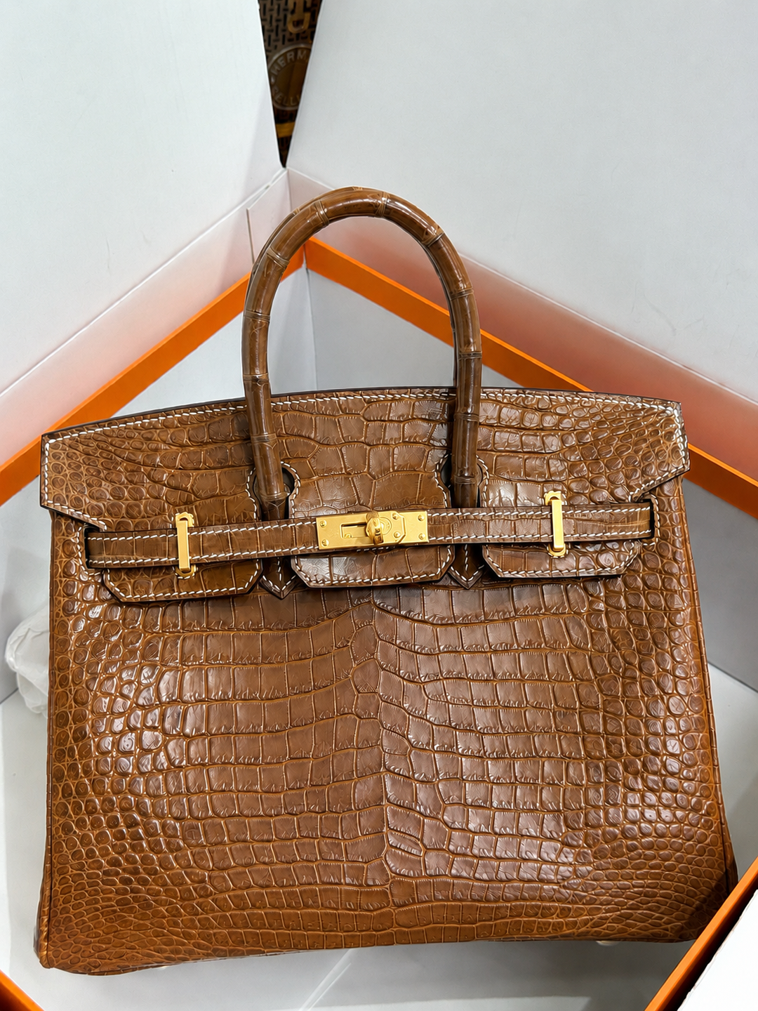 Brown crocodile skin handbag with gold hardware on a white background