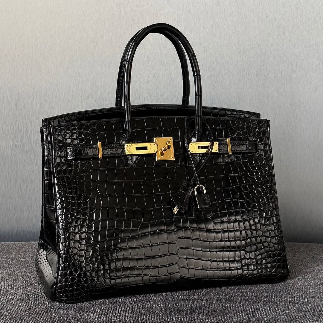 Black crocodile skin handbag with gold hardware on a gray background