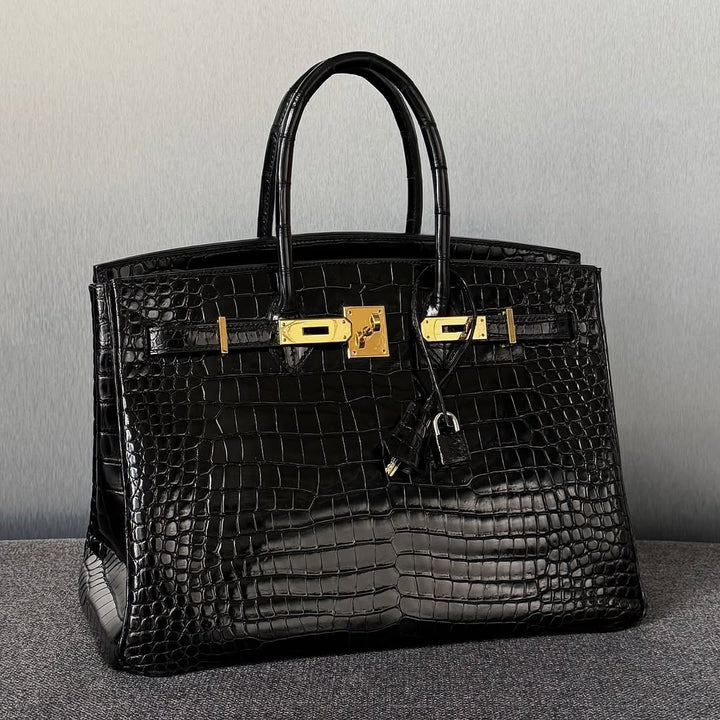 Black crocodile skin handbag with gold hardware on a gray background