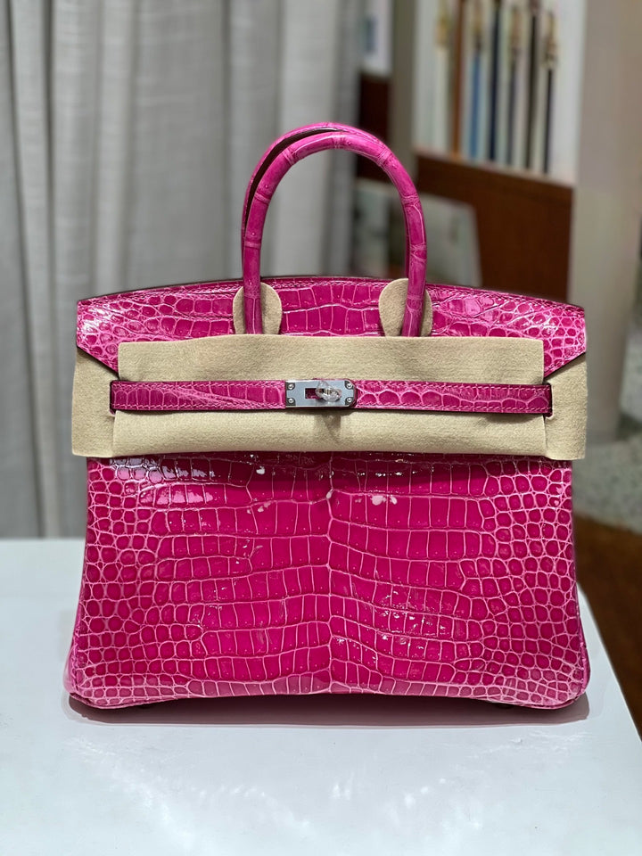Pink crocodile skin handbag with beige leather accents on a white surface.