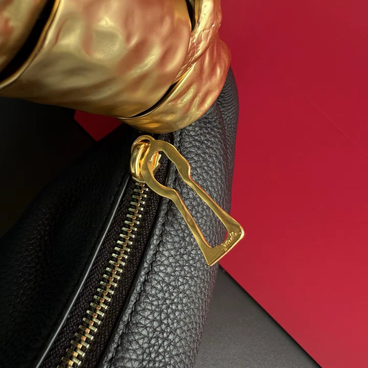 Close-up of a black leather bag with a gold zipper pull against a red background