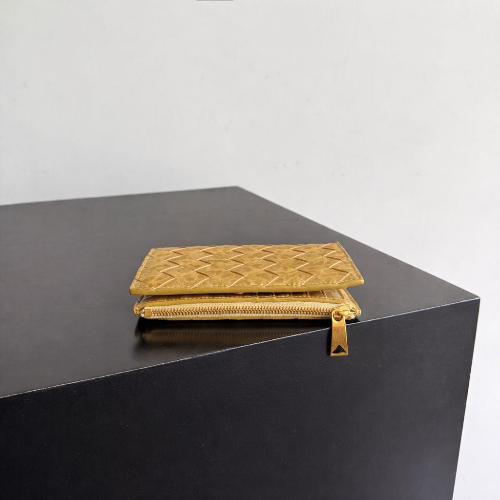 Gold textured wallet on a black surface with a light gray background