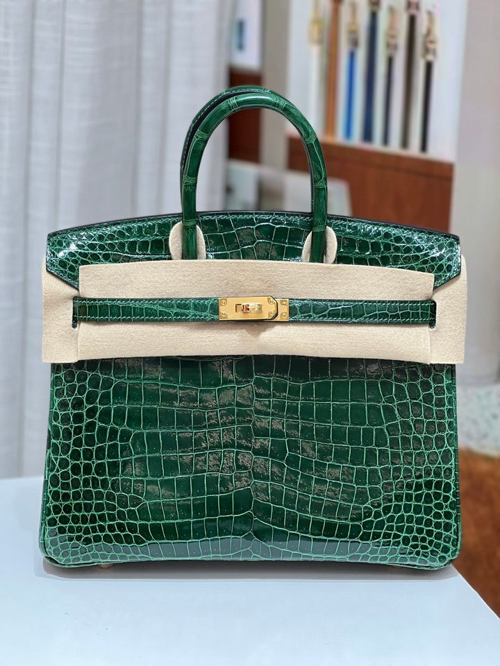 Green crocodile skin handbag with beige leather accents on a light surface.