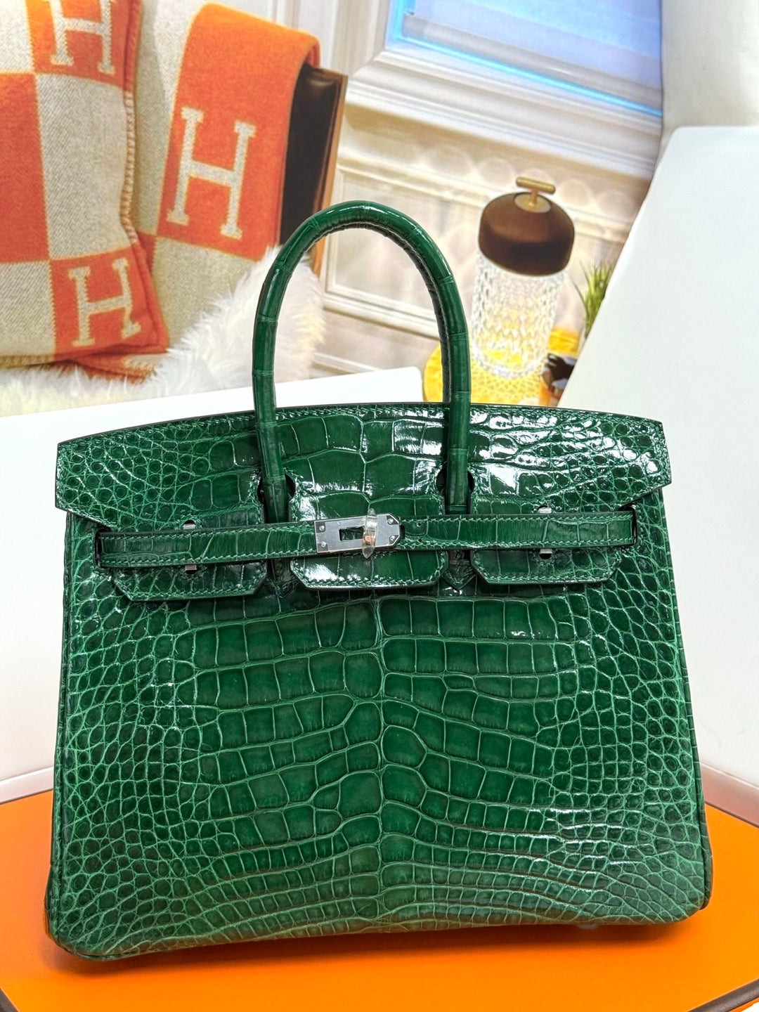 Green crocodile skin handbag on an orange surface with a blurred background