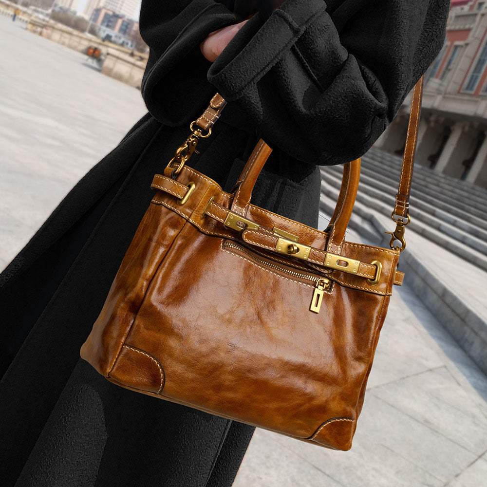 Brown leather handbag with gold accents held by a person in an urban setting.