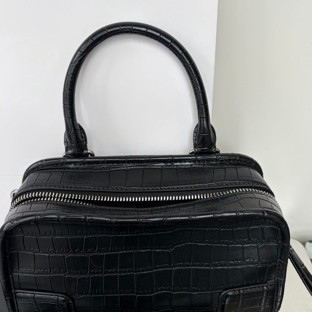 Black crocodile-embossed leather handbag with a top handle and a silver zipper closure, shown against a plain white background.