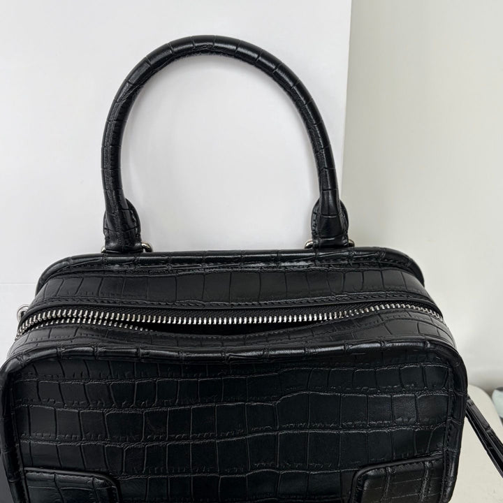 Black crocodile-embossed leather handbag with a top handle and a silver zipper closure, shown against a plain white background.