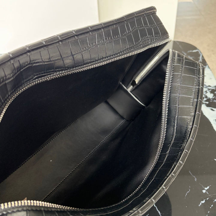 Close-up of the interior of a black crocodile-embossed leather bag, showing a black fabric lining and silver-tone zipper hardware.