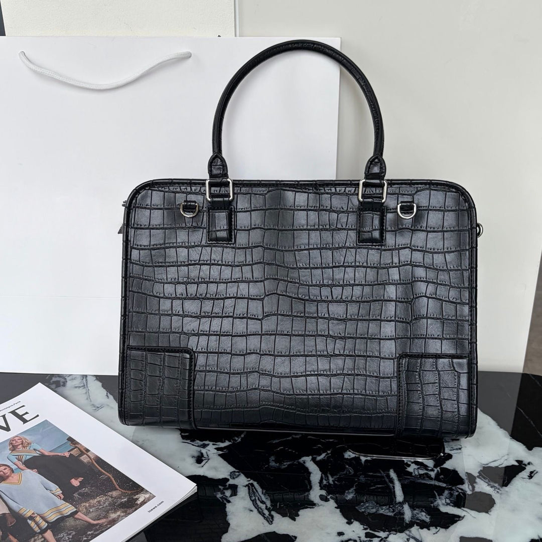 A black crocodile-embossed leather handbag with dual top handles and silver-tone hardware, displayed on a black-and-white marble surface with a white shopping bag and magazine in the background.