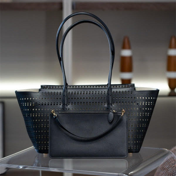 Black perforated handbag on a reflective surface with a blurred background
