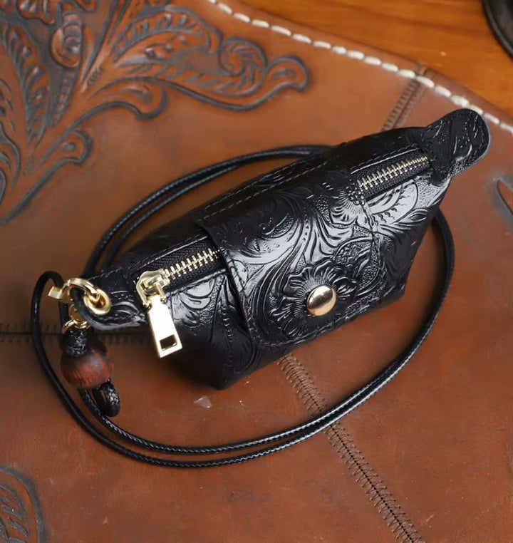 A black tooled leather crossbody bag with gold-tone hardware, resting on a brown leather surface with western-style tooling.