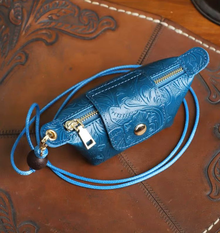 A blue embossed leather pouch with a matching blue cord strap and gold-tone hardware, photographed on a brown tooled leather surface.
