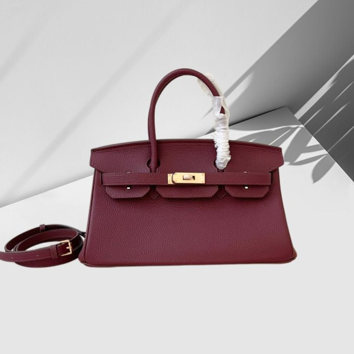 Burgundy handbag with gold hardware on a light gray background