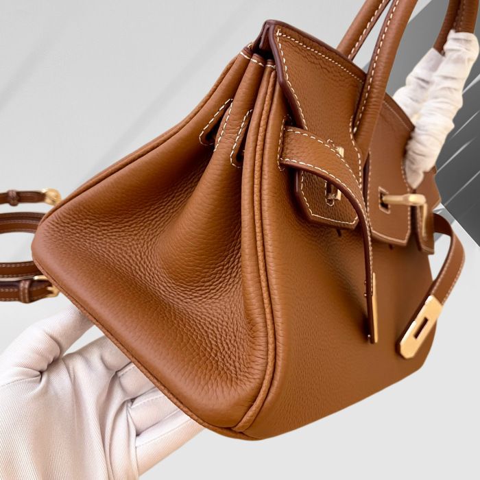 Brown leather handbag held by a gloved hand on a light gray background