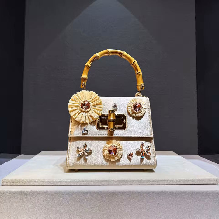 Gold genuine leather box bag with bamboo handle raffia flowers and crystal gems on grey background