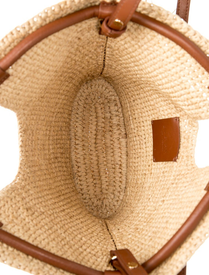 Close-up of a straw handbag with brown leather straps and stitching.