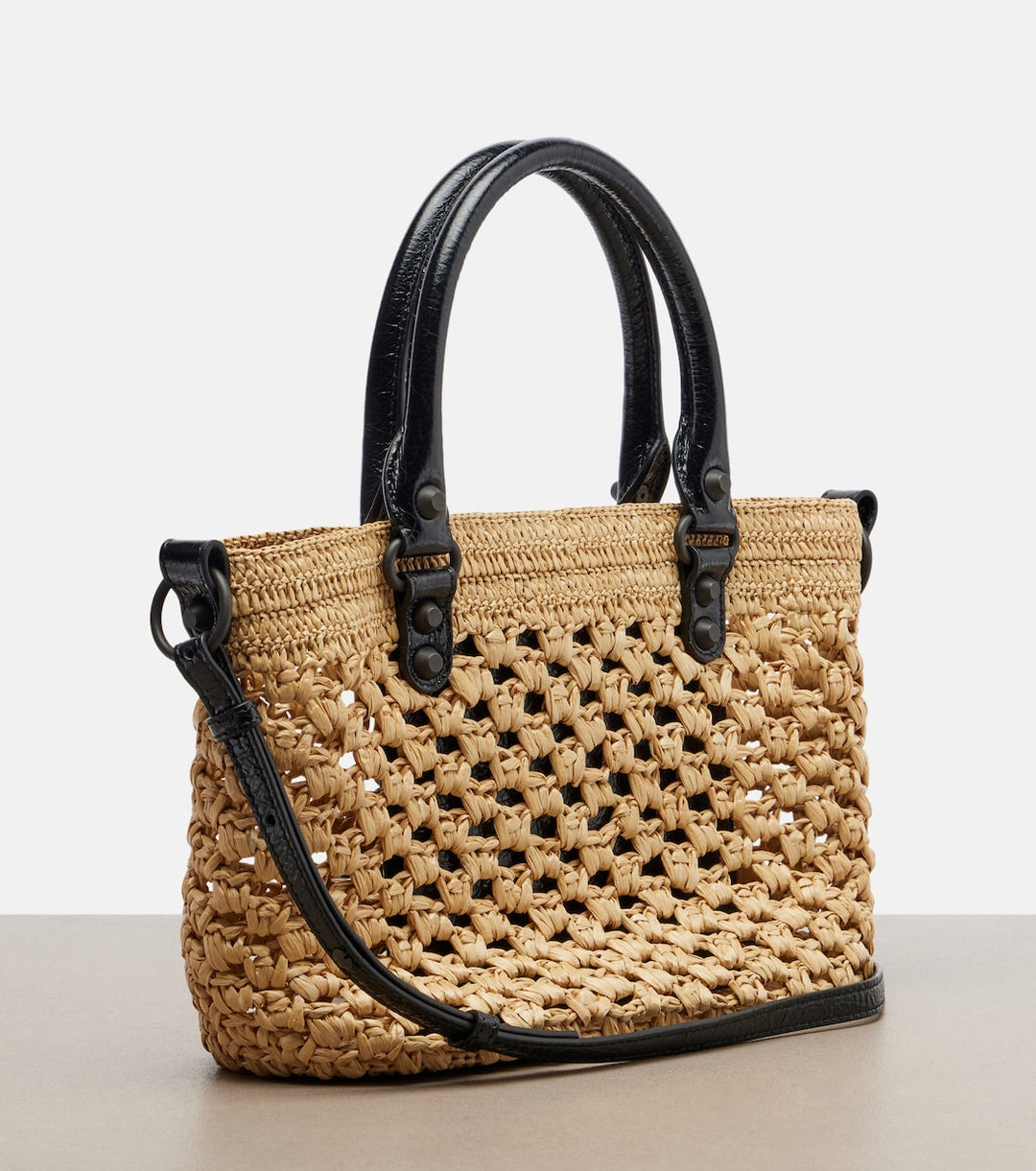 Woven handbag with black handles and strap on a light background