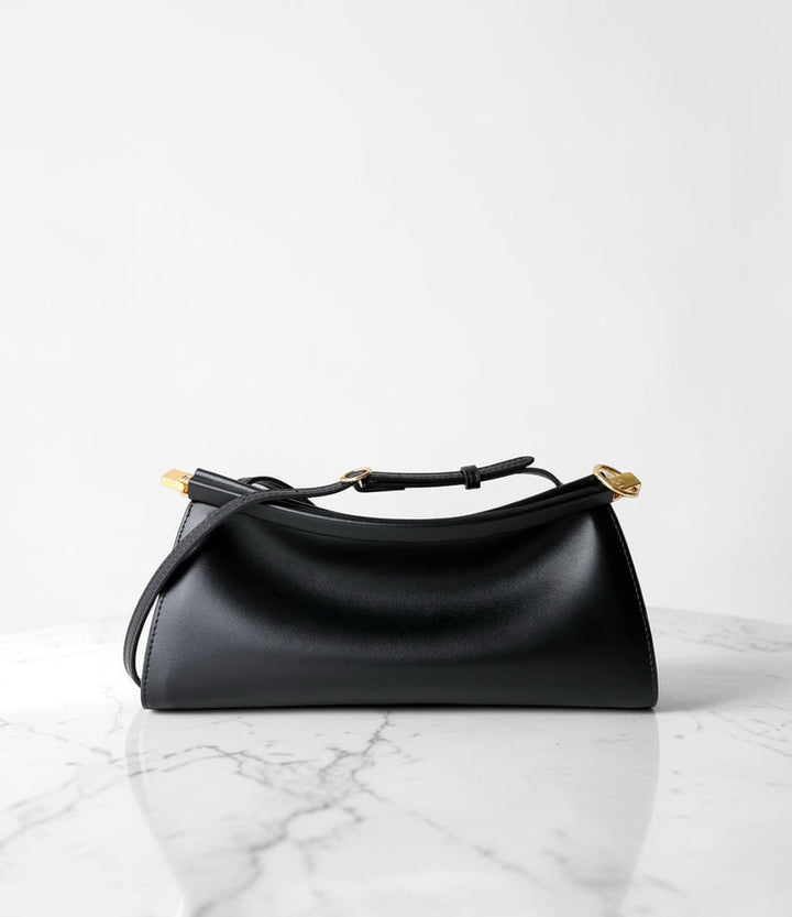 A black leather shoulder bag with gold-tone hardware, resting on a white marble surface against a white background.