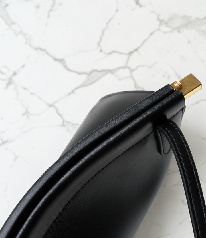 Black handbag with gold clasp on a marble surface