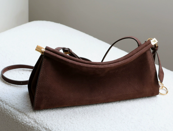 A dark brown pebbled leather shoulder bag with gold-tone hardware, resting on a white textured surface.