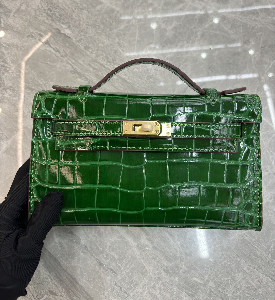 Blue glossy croc-embossed mini flap bag with silver turn-lock hardware on marble surface
