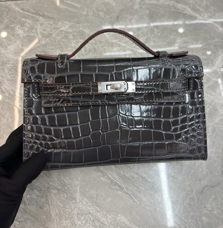 Black crocodile skin handbag with silver hardware on a gray marble surface.