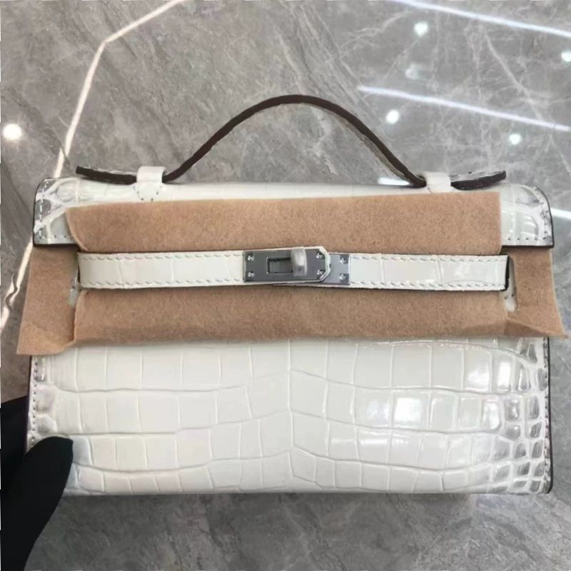 White crocodile-patterned handbag with brown leather accents on a reflective surface