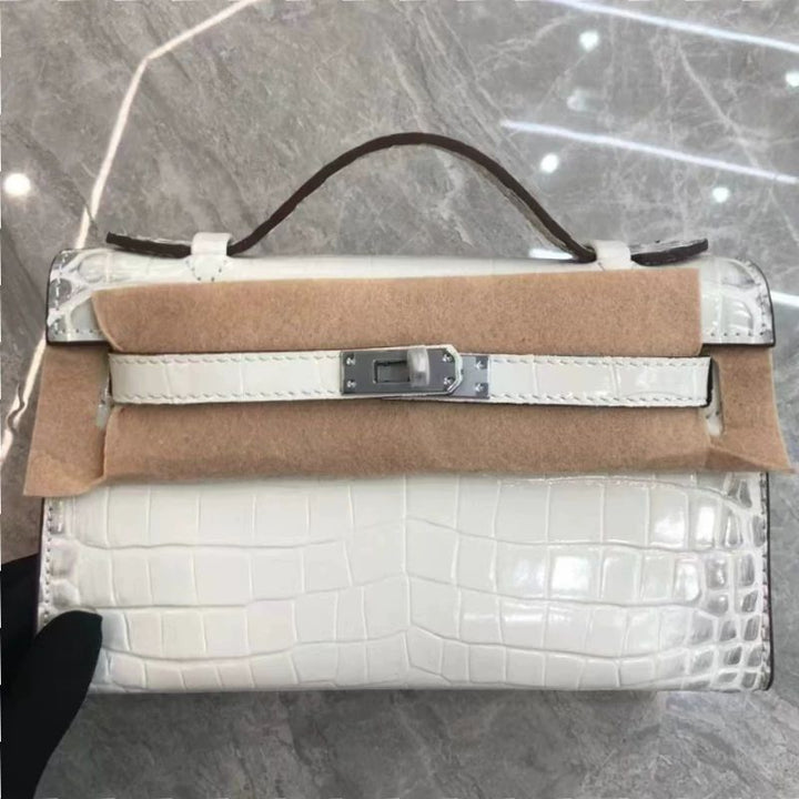 White crocodile-patterned handbag with brown leather accents on a reflective surface