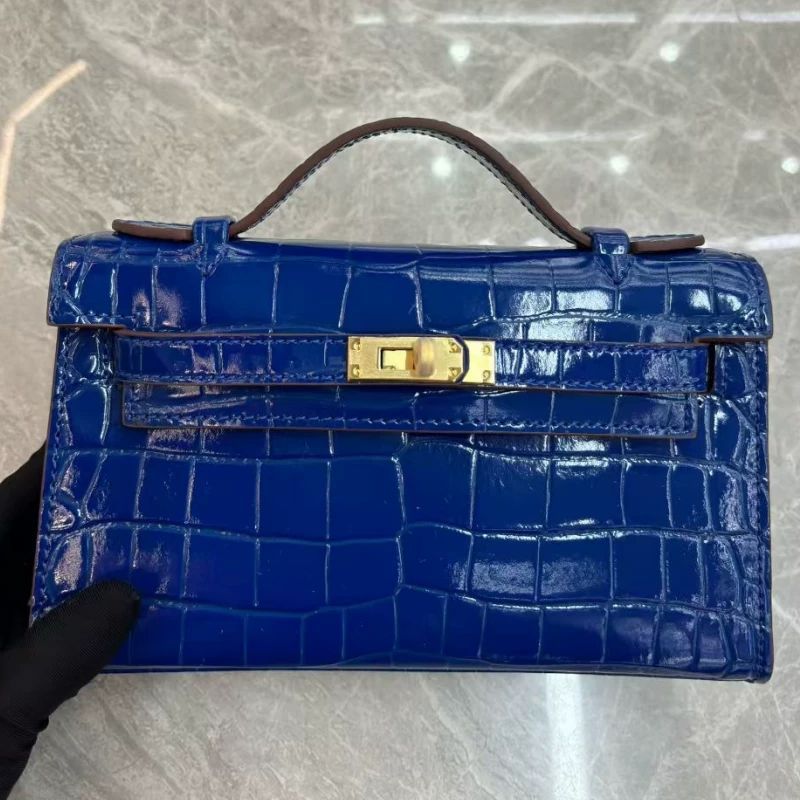 Blue crocodile skin handbag with gold clasp on a reflective surface