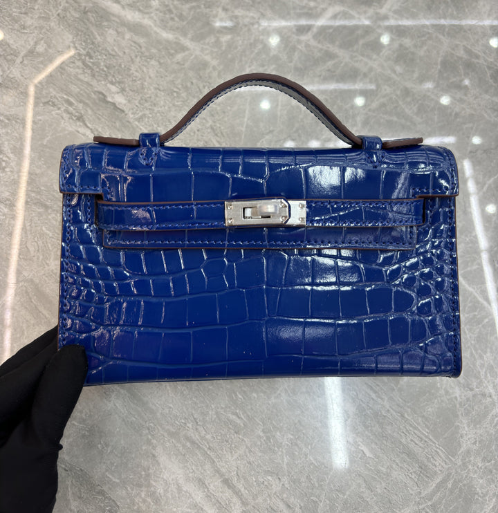 Blue crocodile skin handbag with a silver clasp on a gray marble surface