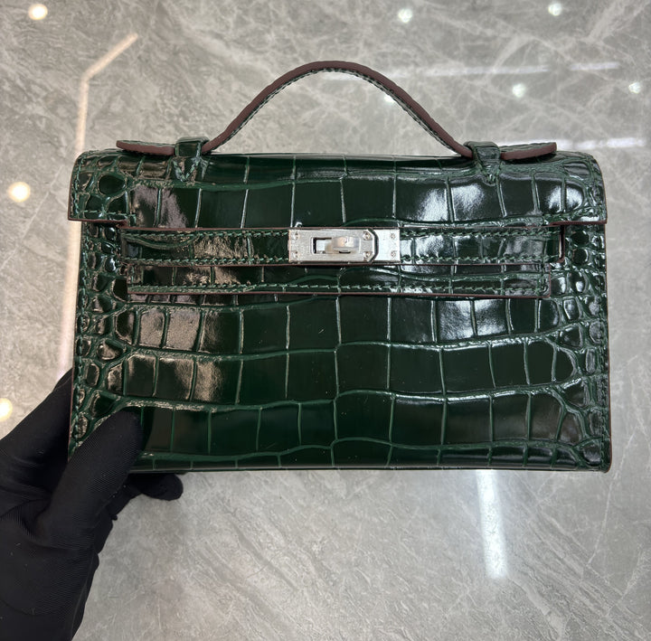 Green crocodile skin handbag held by a gloved hand on a reflective surface