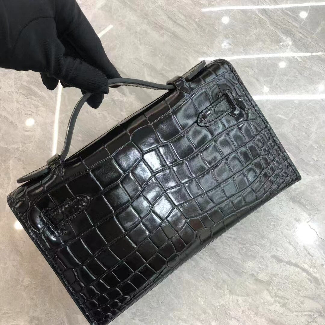 Black crocodile-patterned handbag held by a gloved hand on a reflective surface