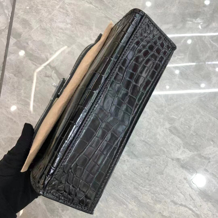 Black crocodile-patterned wallet held by a gloved hand on a reflective surface