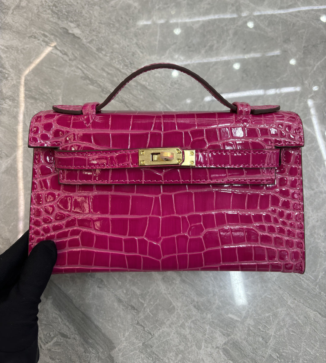 Namrico glossy blue crocodile-embossed mini bag held in hand on marble floor setting
